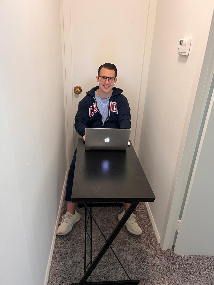 Drew Speckman ’20 sitting in a small apartment hallway at a table with little room to move.