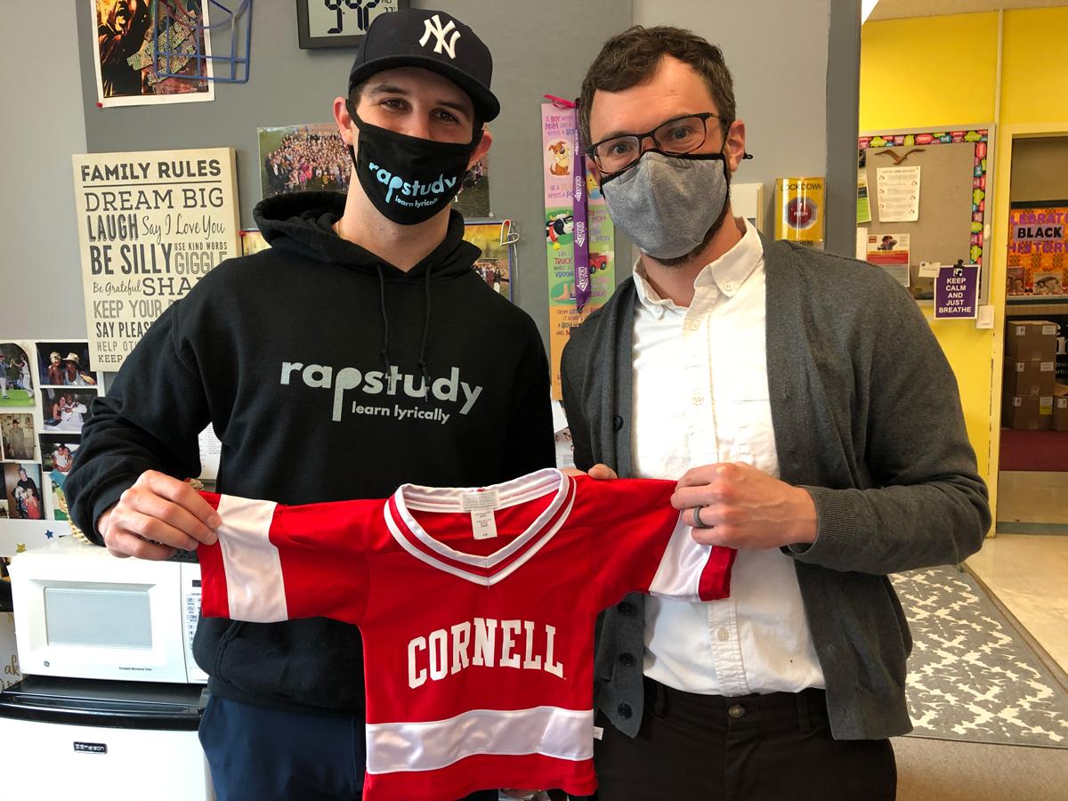 Drew Speckman ’20 in a classroom holding a child sized Cornell hockey shirt