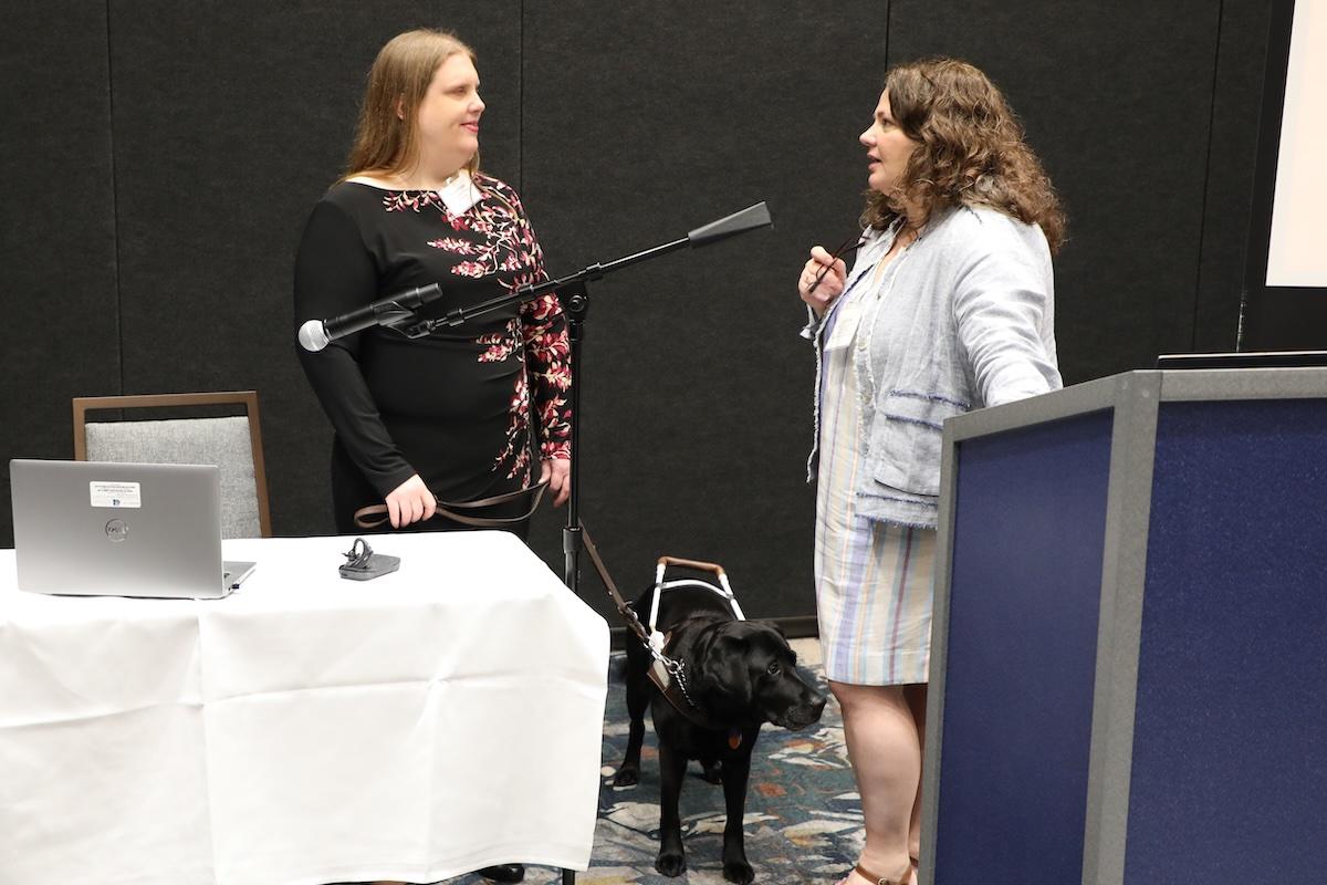 Meghan Parker and Ellice Switzer, giving a presentation. Parker is accompanied by a service dog