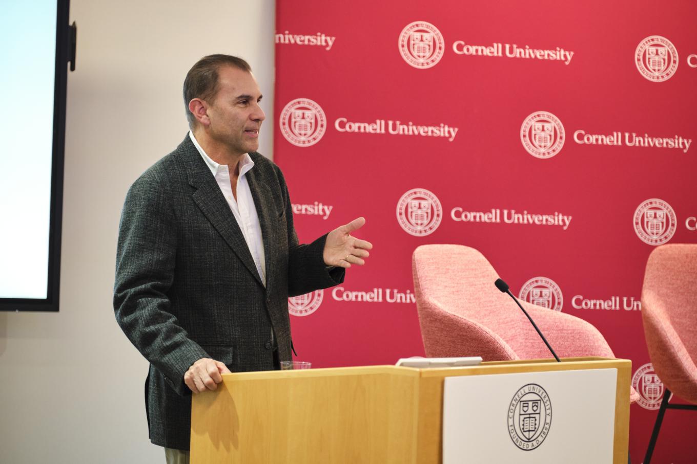 GLI Board Member Duncan Scott addresses the 2025 GLI conference in New York CIty, as he stands in front of a red background with Cornell University on it.