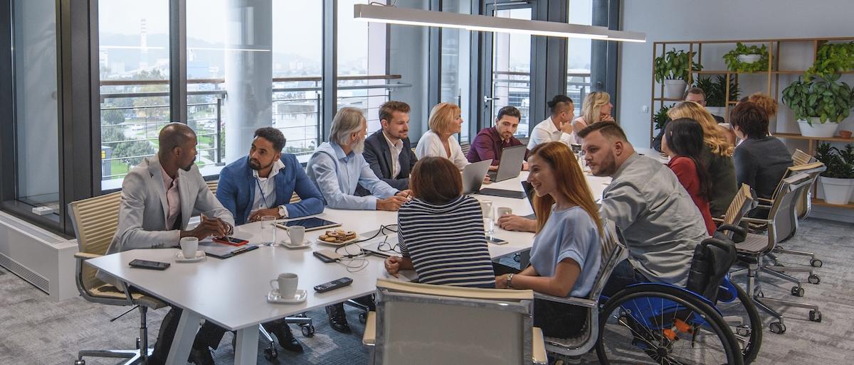 Employees sitting at a conference room table. One employee is sitting in a wheelchair.