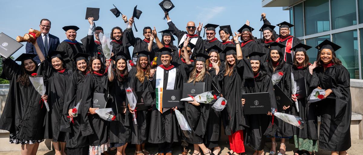 group of EMHRM recent graduates smiling and wearing full regalia