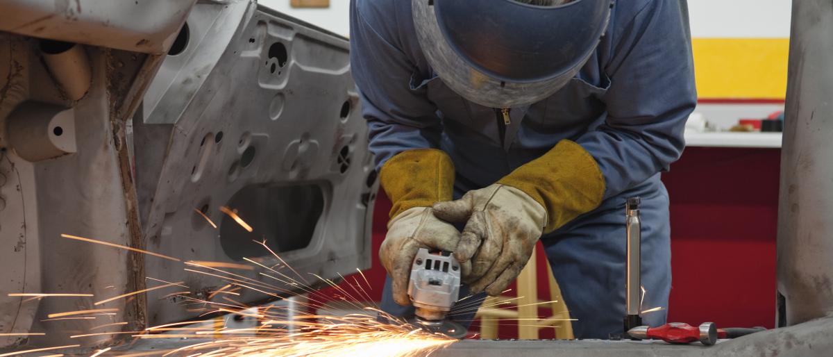Worker bent over car welding a vehicle