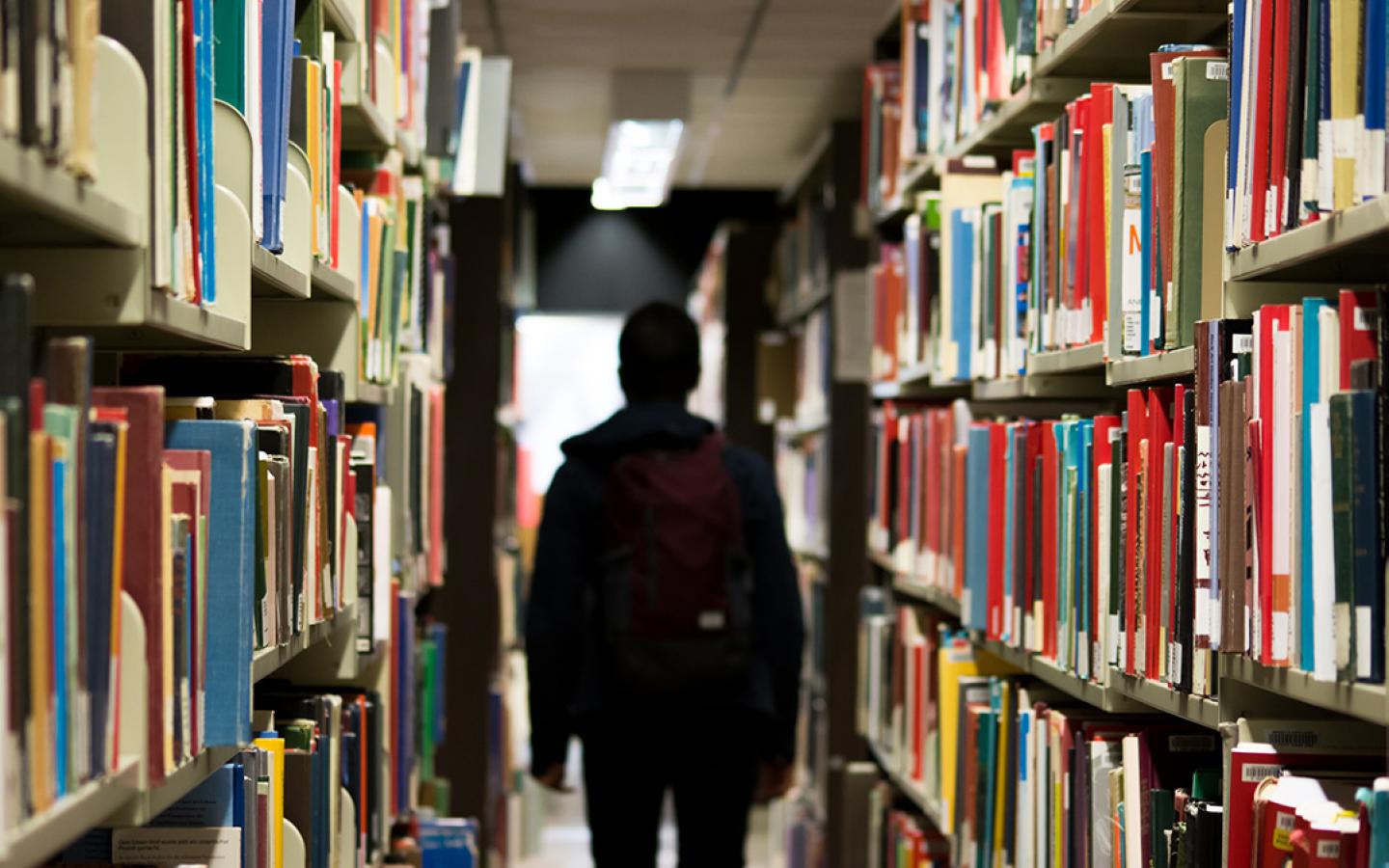 person walking through hallway lined with books