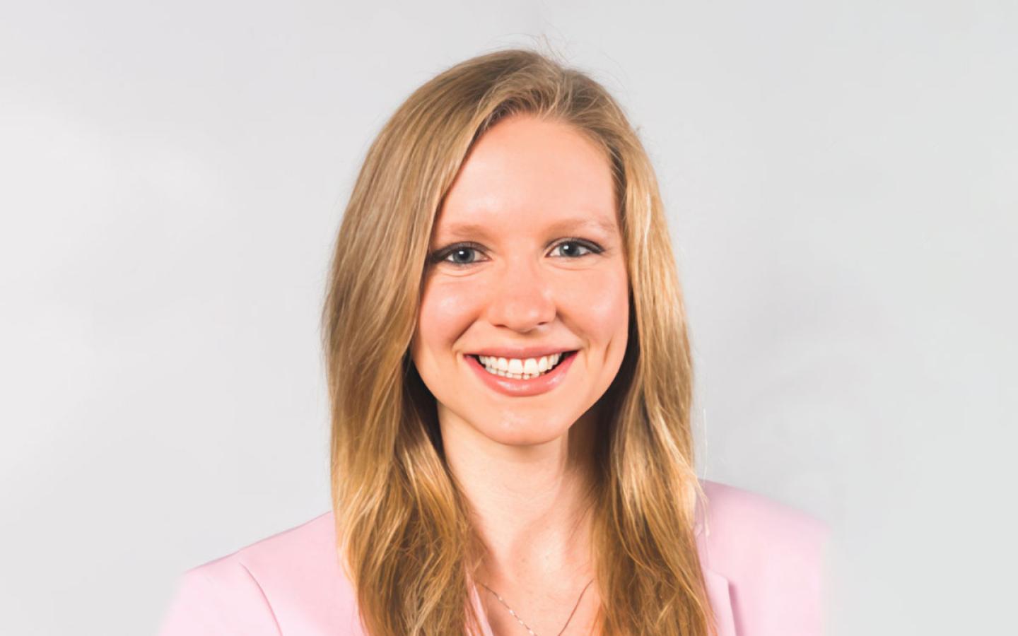 Katie Brendli Brown. Katie is white, has long, blonde hair, and is smiling and wearing a pink jacket.