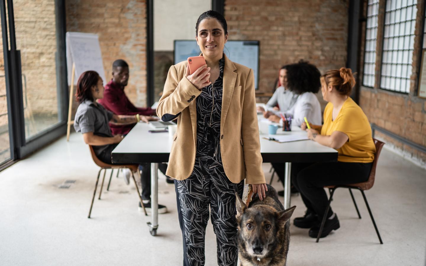A visually impaired businesswoman using smartphone in an office with guide dog