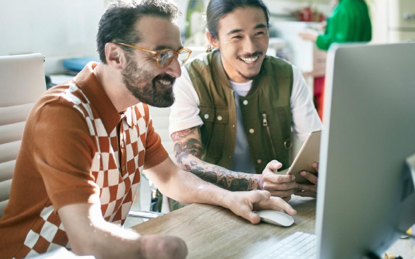 Two veterans in the workplace collaborate while looking at a computer