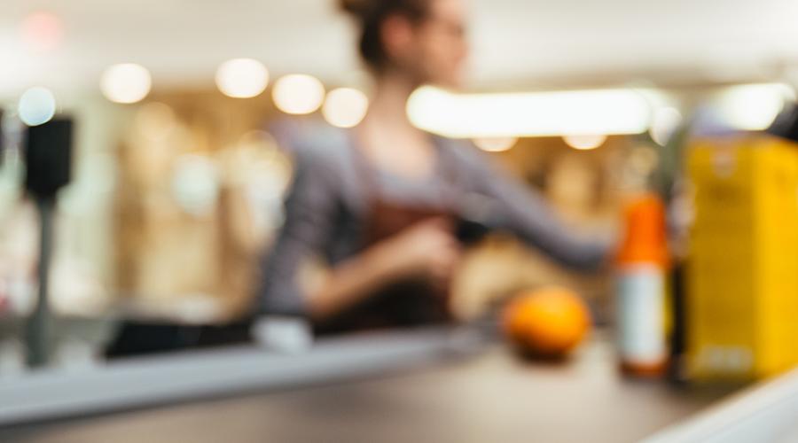 Young female cashier checking items on a conveyor belt.