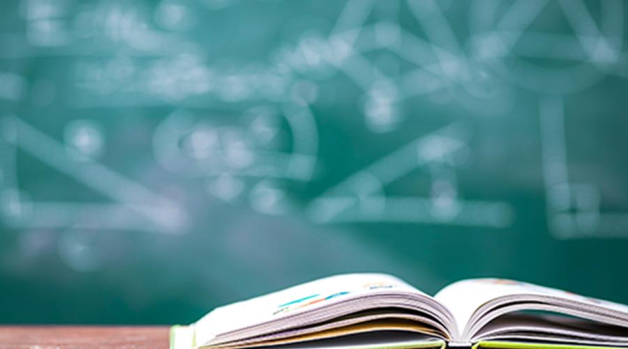 An open book setting on a desk with a chalkboard showing math illustrations in the background.