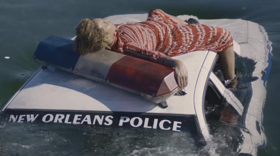 Person laying on a police car that says New Orleans Police which is sinking 