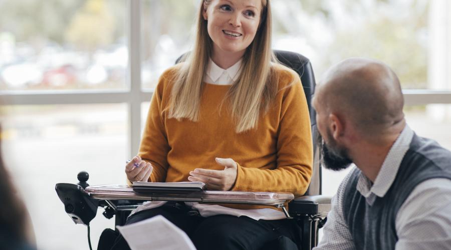 Young woman in a wheelchair talks with a co-worker