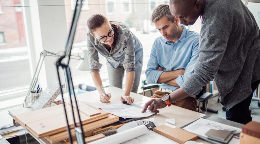 Three employees in a sunny office reviewing a diagram together