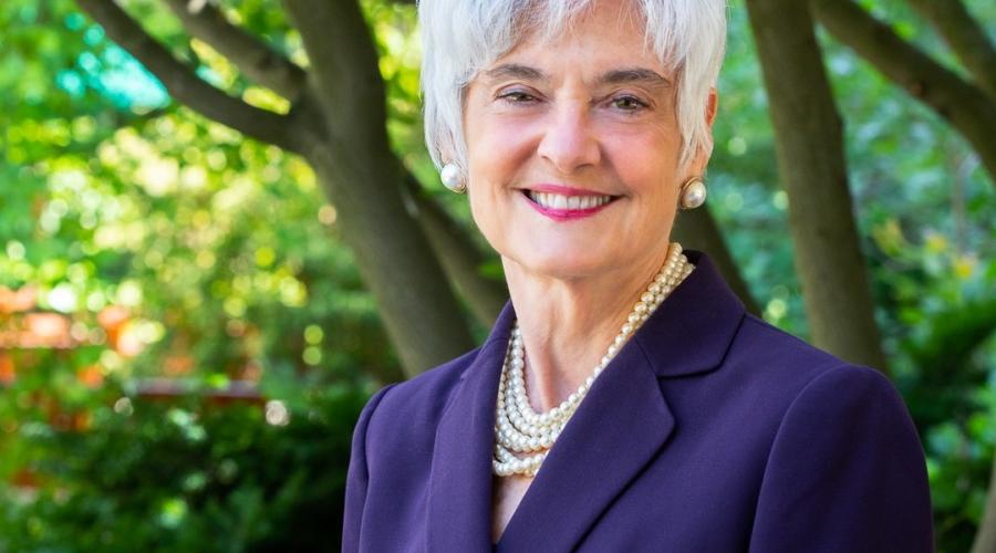 Susanne Bruyère, wearing a purple blazer with several strands of white pearls and matching earrings