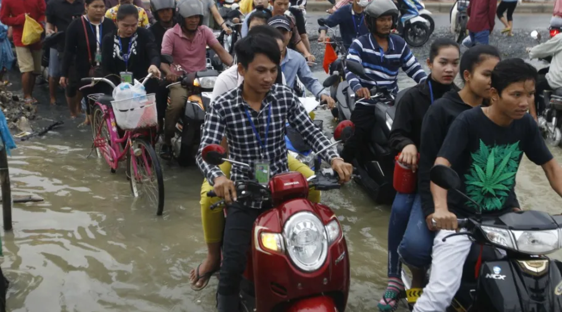 Person riding scooter through crowded, flooded street. 