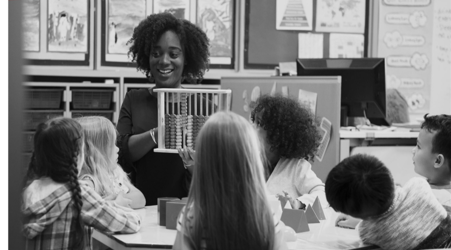 A child care worker reads to young children who follow along in the book she holds.