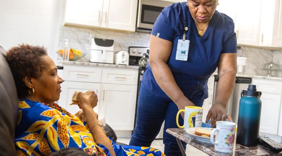 Photo of a home healthcare worker administering medication to a woman who is seated and eating.