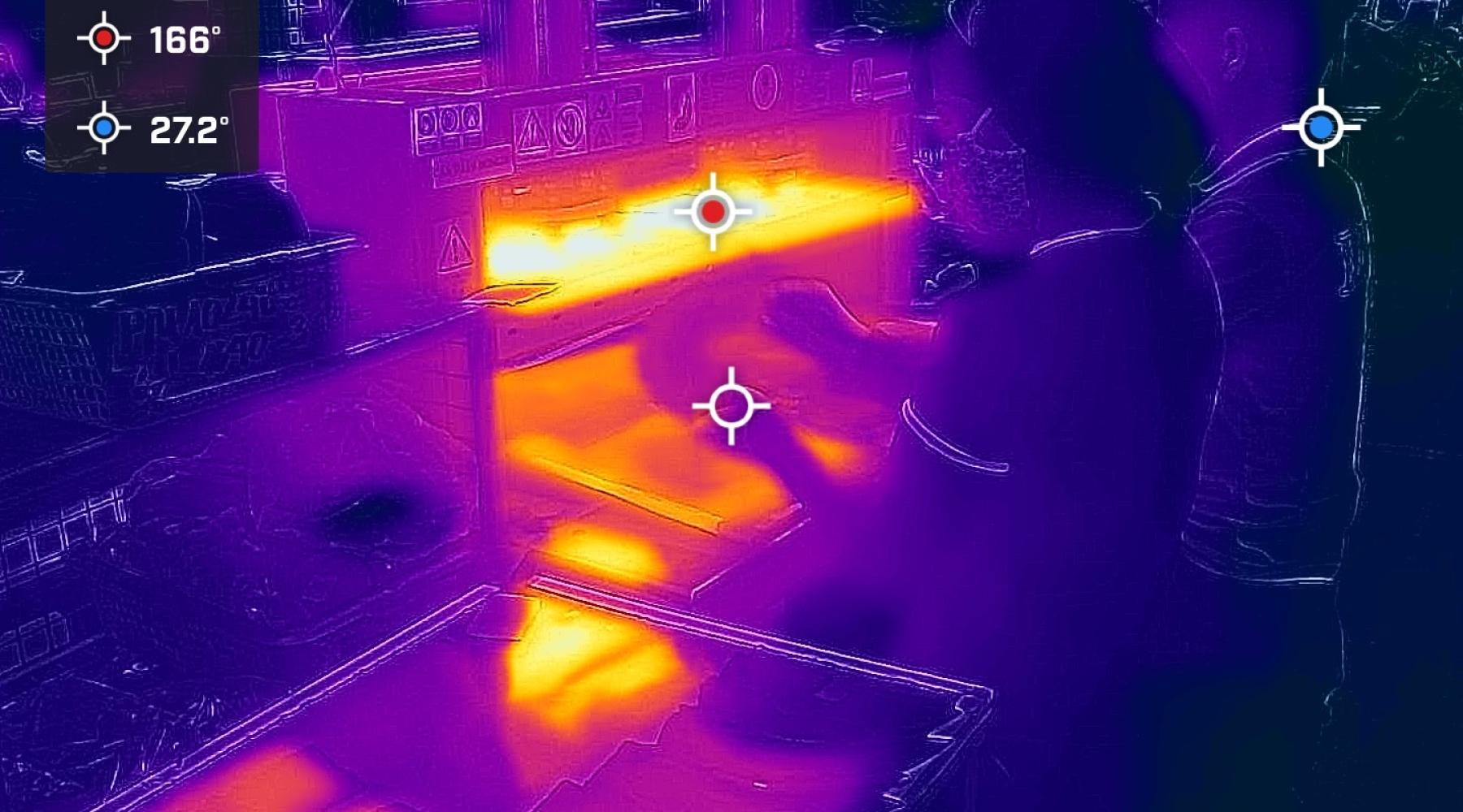 A thermal image of a worker at a station in a garment factory, showing the high heat levels through brighter orange colors at their workstation.