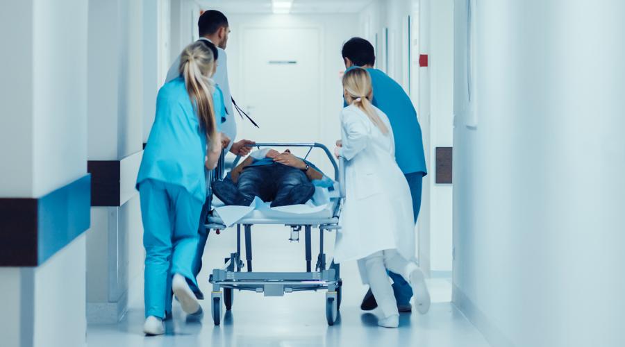 Emergency department doctors and nurses push a gurney stretcher with seriously injured person.