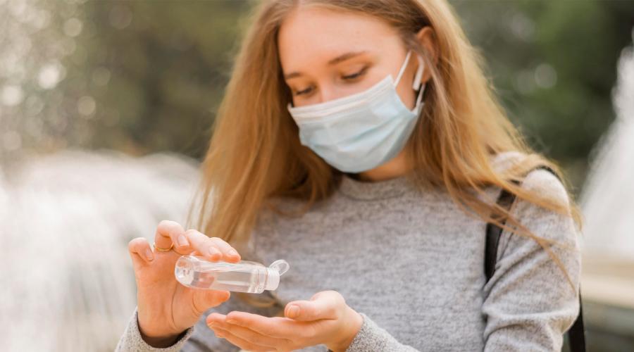 A woman wearing a mask applies sanitizer to her hands