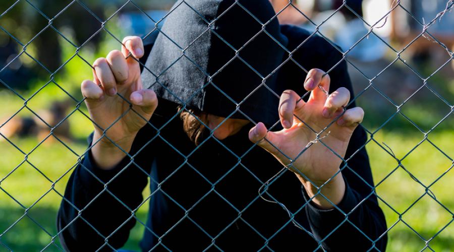 Teenage boy holding wired fence at correctional institute.