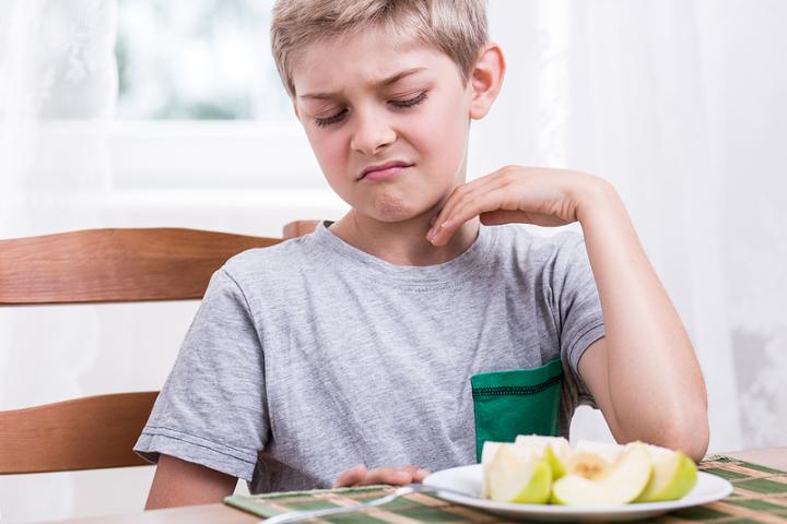 A young boy refusing to eat an apple