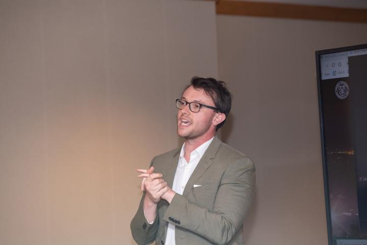 A man stands talking with his hands clasped