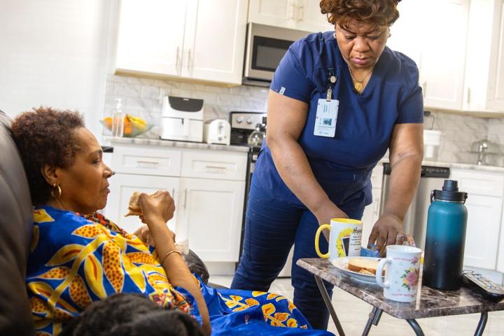 Photo of a home healthcare worker administering medication to a woman who is seated and eating.