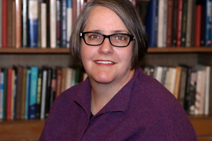 Middle-aged white woman with short brown hair and glasses, wearing a dark magenta top