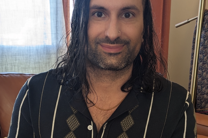 Image of a man with dark hair smiling at the camera, wearing a green button up shirt.