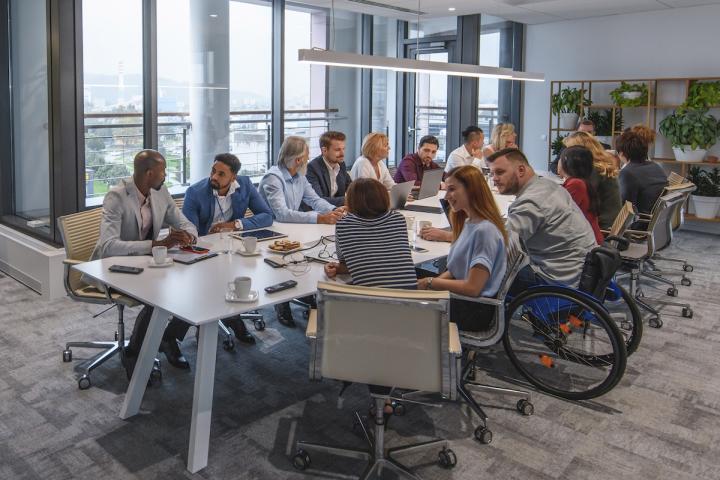 Employees sitting at a conference room table. One employee is sitting in a wheelchair.