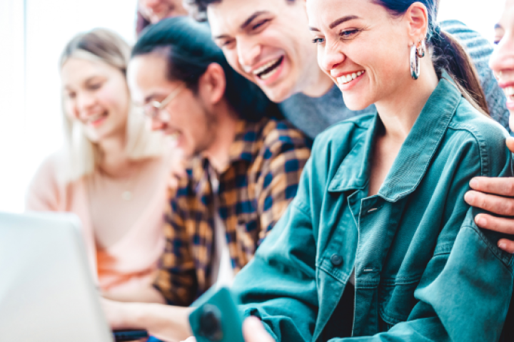 Image of a group of smiling young professionals gathered around a laptop.