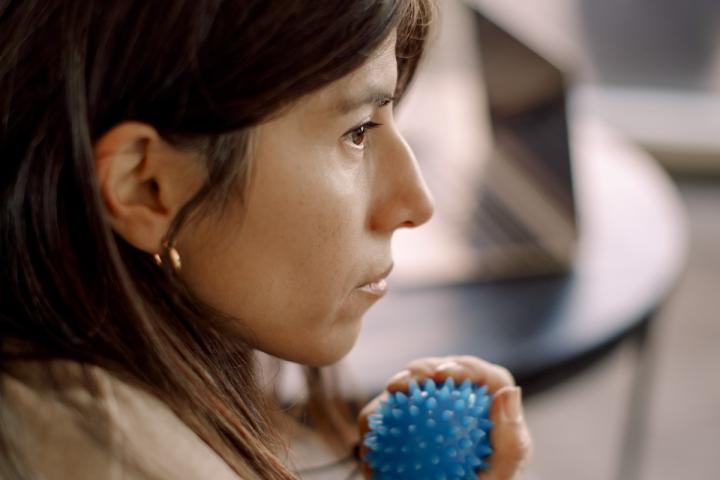 A person squeezes a small blue stress/massage ball