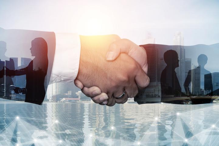 Two business professionals shaking hands in the foreground, overlaid with silhouettes of people networking and a modern city skyline, symbolizing partnership, collaboration, and professional relationships.