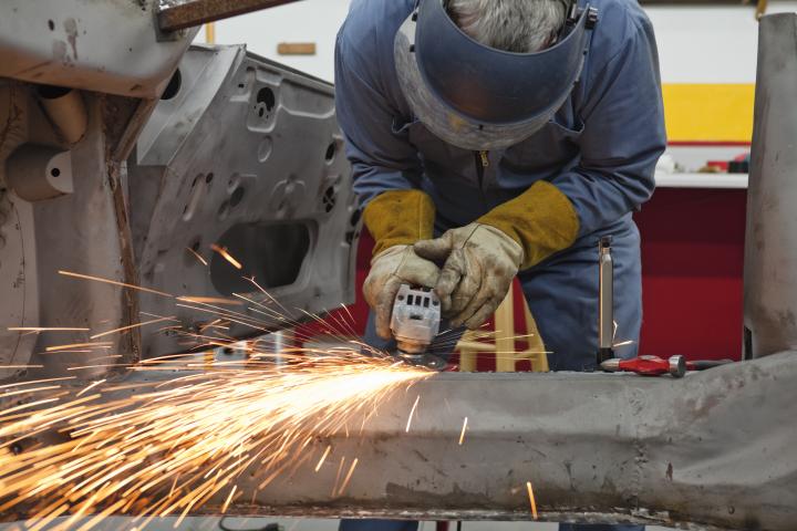 Worker bent over car welding a vehicle