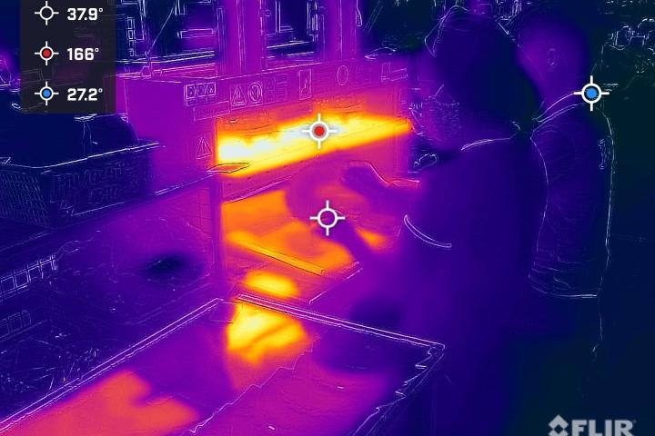 A thermal image of a worker at a station in a garment factory, showing the high heat levels through brighter orange colors at their workstation.
