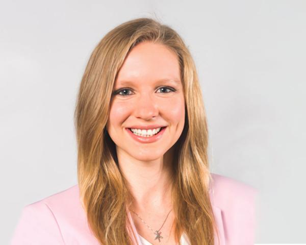 Katie Brendli Brown. Katie is white, has long, blonde hair, and is smiling and wearing a pink jacket.