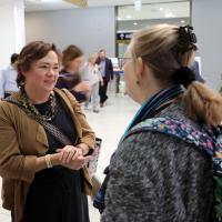 Yang-Tan Institute executive director Wendy Strobel Gower smiles while chatting with a DREAM attendee. Strobel Gower is professionally dressed in chunky jewelry, black dress and tan wrap; the attendee is wearing a blue scarf over a gray top and a backpack with a floral design.